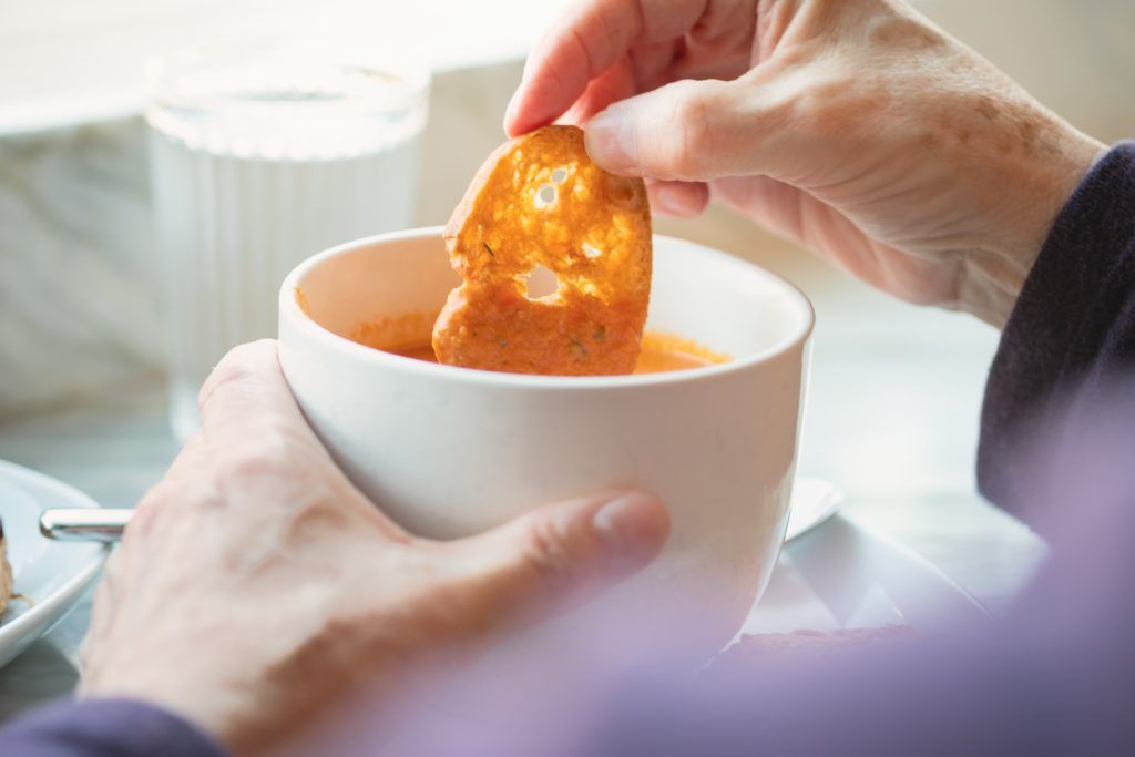 An elderly person dipping a crisp bread into a bowl of soup, highlighting nutritious meals in care home