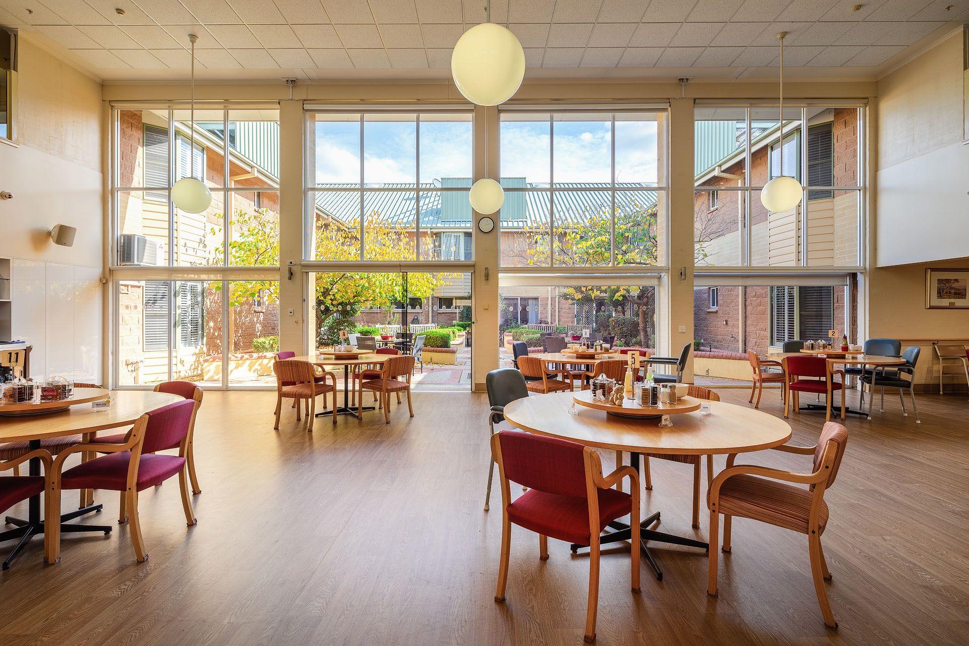 A bright communal dining area at St Catherine’s care home with wooden tables, chairs, and large windows overlooking gardens